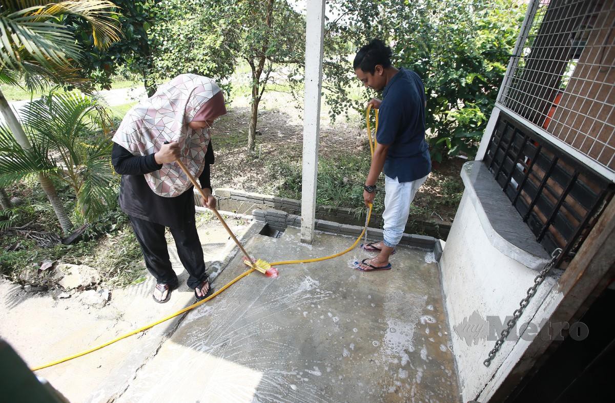 SYAKILA bersama suaminya membersihkan rumah mereka yang dilanda banjir semalam susulan hujan lebat lebih sejam. FOTO Genes Gulitah.
