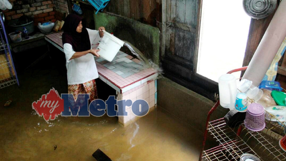 PENDUDUK, Norihah Awang, 57 membersih dapur rumahnya yang hampir tenggelam walaupun banjir masih belum surut sepenuhnya di Kampung Kolam. FOTO Nik Abdullah Nik Omar