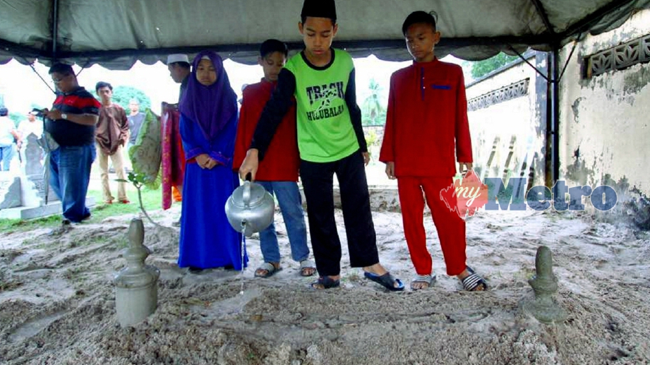 ANAK-anak arwah Norman vokalis kumpulan Panji menyiram air di pusara ayah mereka yang dikebumikan di tanah perkuburan islam Syed Yahaya, Jalan Nibong, hari ini. FOTO Rosli Ilham