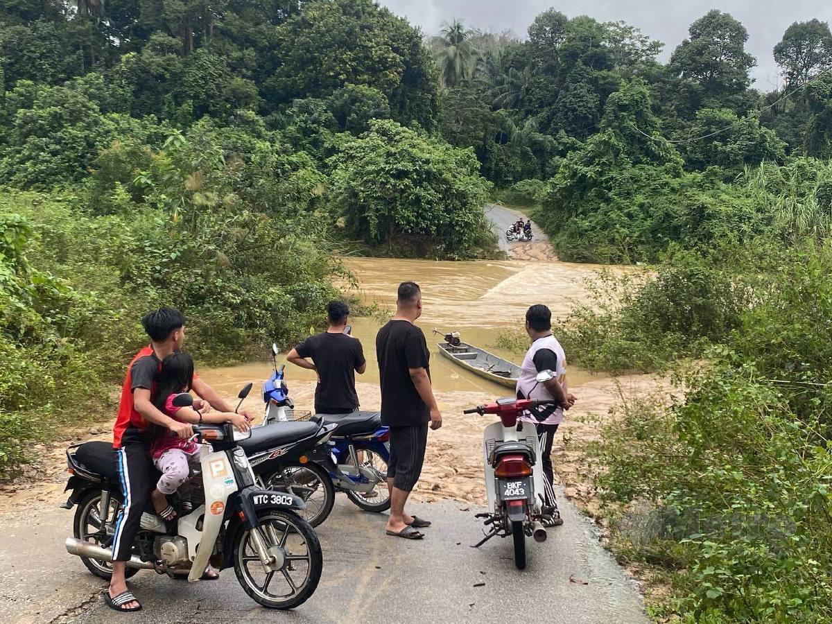 Penduduk meninjau keadaan di Jambatan Kampung Belanga ditenggelami Sungai Pahi sejak Selasa lalu susulan hujan lebat mengakibatkan paras air meningkat mendadak. FOTO Hazira Ahmad Zaidi