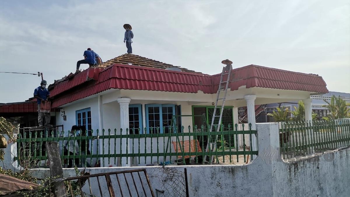 PEKERJA membaiki bumbung rumah yang terjejas akibat ribut di Kampung Tawas. FOTO Balqis Jazimah Zahari