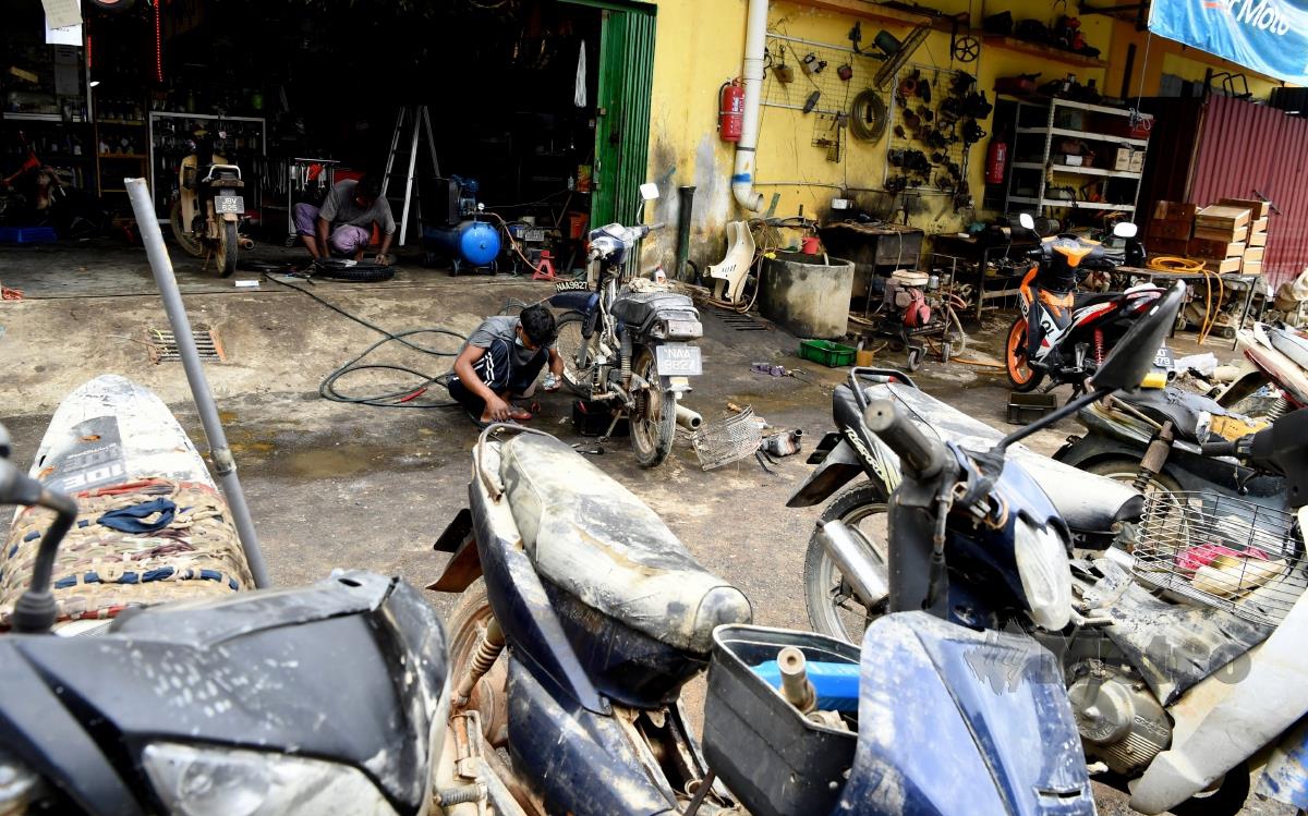 Pekerja sebuah kedai motosikal membersihkan motosikal pelanggannya yang dipenuhi lumpur susulan kejadian banjir. FOTO BERNAMA