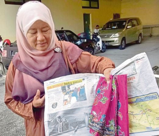Zawiyah menunjukkan berita kematian seorang anggota tentera pada akhbar yang membungkus kain batik  dibeli anaknya yang maut dalam kemalangan, kelmarin.