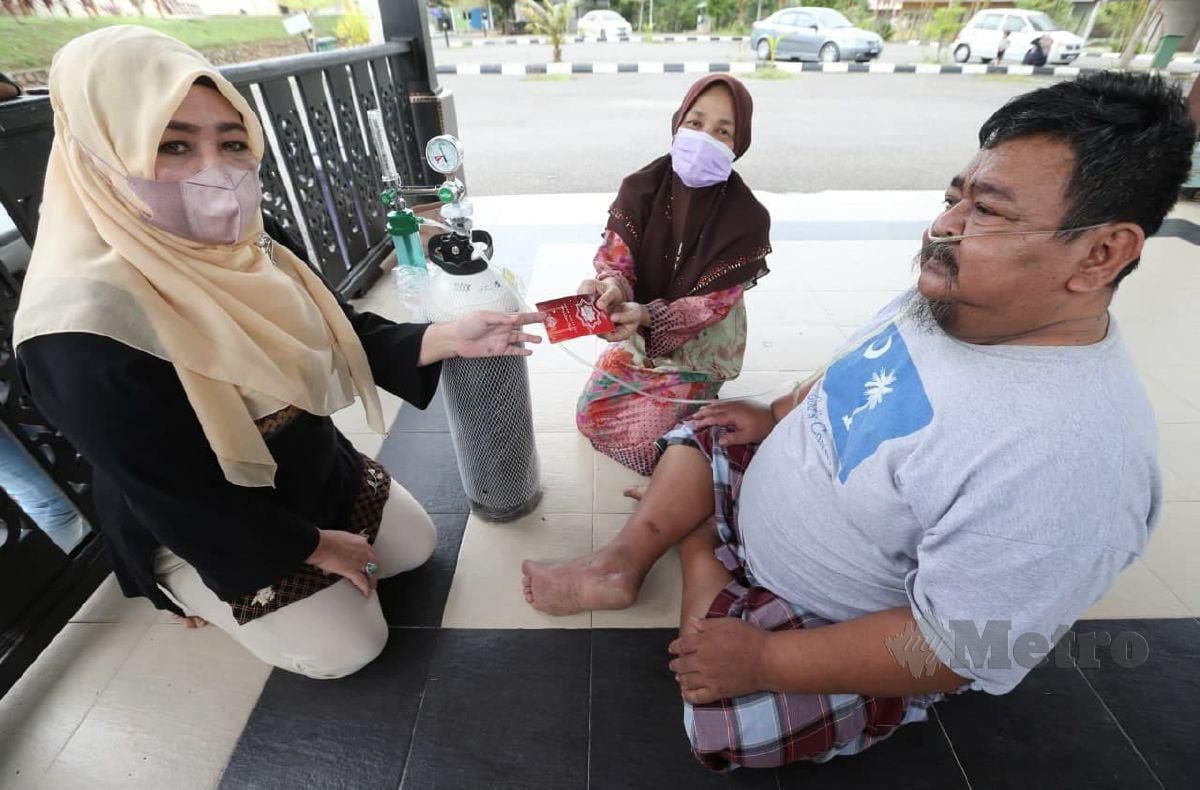 CHE Norhayati (kiri) menghulurkan wang zakat kepada Mohd Razi yang ditemani Nor Hazliza ketika ditemui di Kampung Lundang. FOTO NIK ABDULLAH NIK OMAR