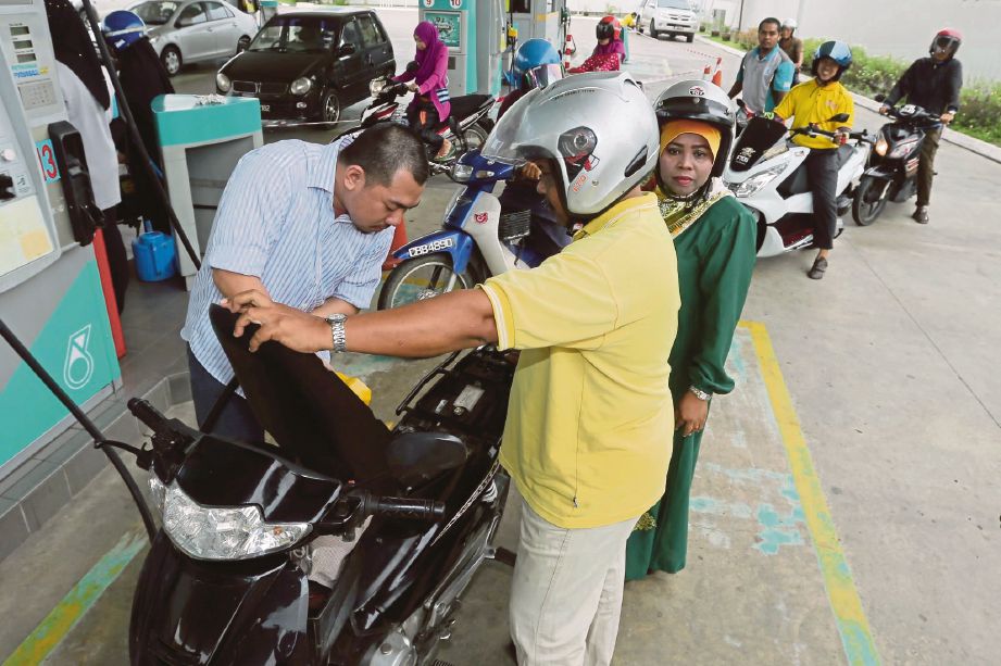 MOHD Harmizuan   (kiri) mengisi petrol percuma  kepada penunggang motosikal   di Stesen minyak Petronas Pasir Pekan.  