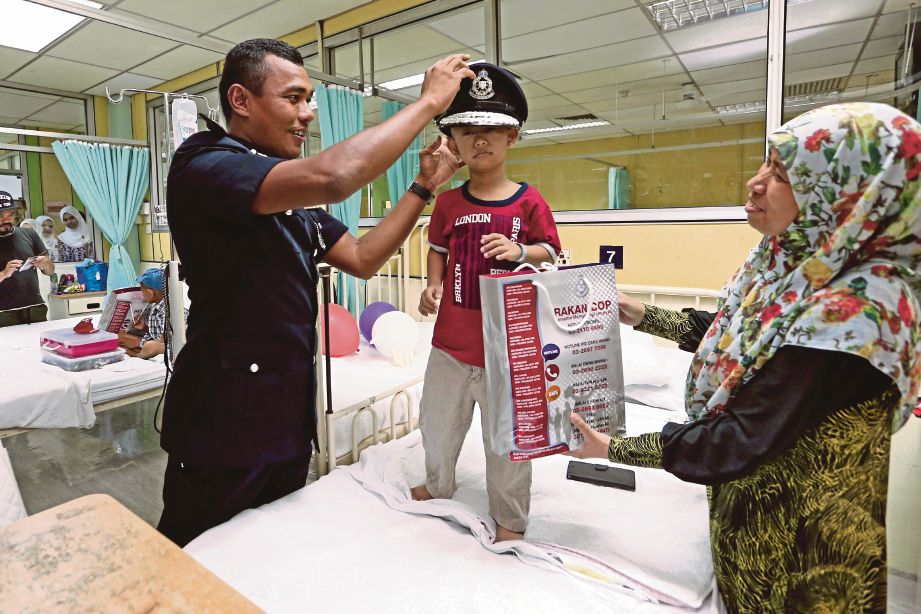 MOHD Sukri memakaikan topi polis kepada Muhammad Nur Fa’iz di Unit Pediatrik HKL.