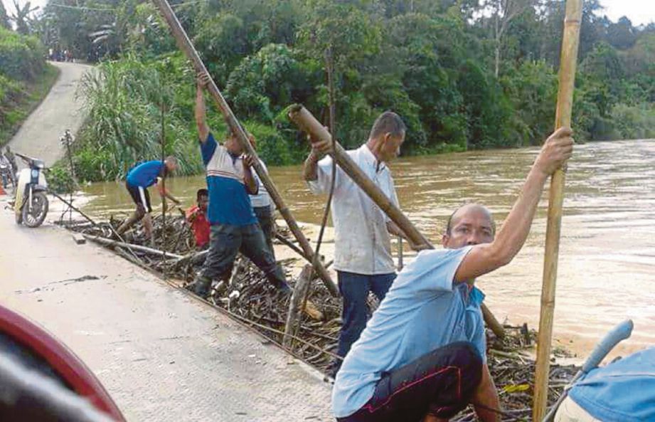 PENDUDUK kampung mengadakan gotong-royong membersihkan sisa kayu yang tersekat di jambatan.