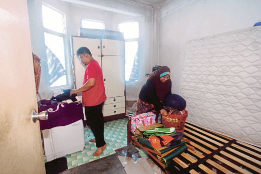 Ismail bersama Maimon mengemas pakaian dan peralatan rumah yang basah terkena hujan setelah atap rumah diterbangkan ribut.
