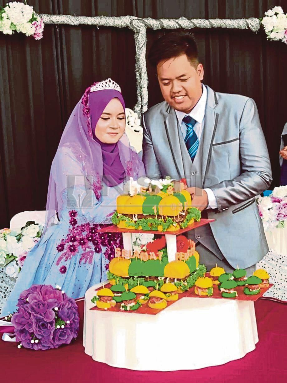 PASANGAN pengantin memotong burger kek yang menjadi tarikan tersendiri pada majlis perkahwinan mereka. FOTO Nur Izzati Mohamad