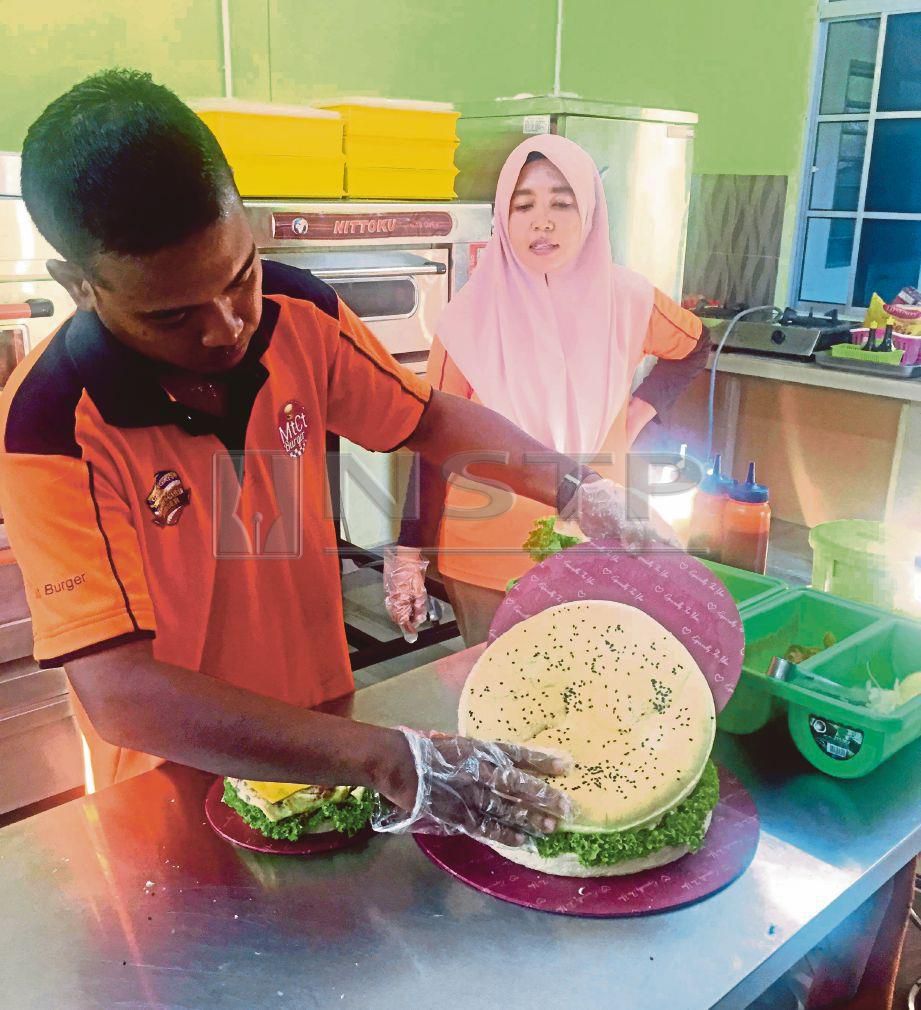 MUHAMAD Hasseni menyiapkan tempahan burger berbentuk kek   sambil disaksikan  Siti Umairah di bengkel pasangan terbabit dekat Kampung Permatang Rambai, Kepala Batas. FOTO Nur Izzati Mohamad