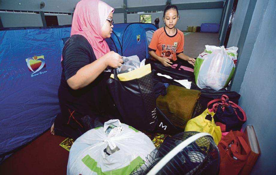 MAS Ayraa Qursiah (kiri) bersama adiknya mengemas barang sebaik tiba di pusat perpindahan mangsa banjir di Dewan Palembang, Kapar. 