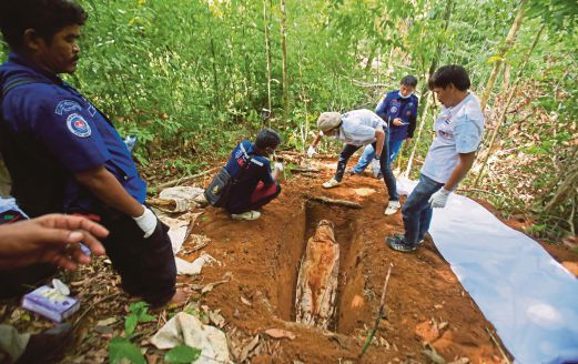 PASUKAN penyelamat mengeluarkan jenazah yang ditemui dalam kubur cetek berhampiran pekan Padang Besar Thailand.  