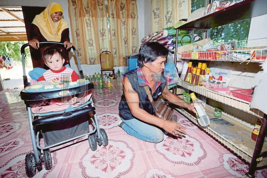ISMAIL menyusun barang jualan di kedai runcitnya sambil diperhatikan  Sofiah dan anak mereka,  Muhammad Solehudeen.