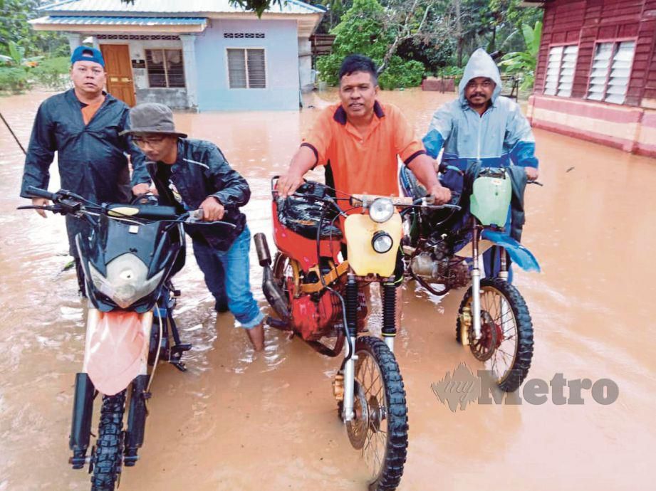 FAIZUL  (kanan) bersama penduduk memindahkan motorsikal yang terlibat banjir di Kampung Lembah Bakti, Labis. 