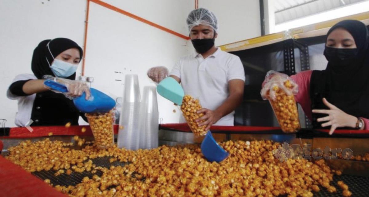 MUHAMAD Azamuddin (tengah) bersama pekerjanya mengisi bertih jagung ke dalam bekas ketika ditemui di kilangnya.