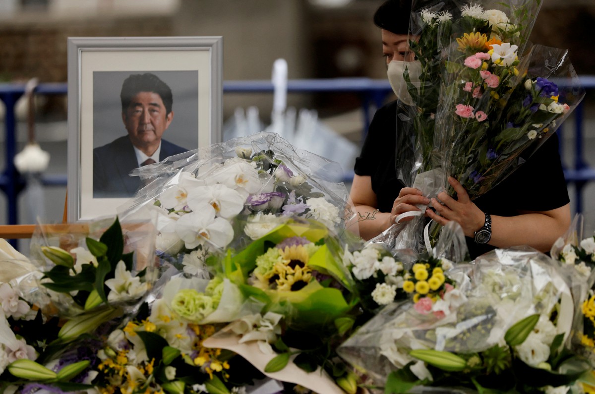 SEORANG penduduk Jepun meletakkan bunga di potret bekas Perdana Menteri Shinzo Abe yang maut ditembak minggu lalu. FOTO Reuters.
