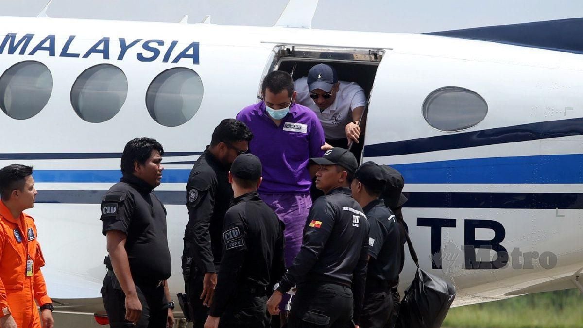 SUSPEK yang memakai baju lokap ungu diiringi polis turun dari pesawat di Pangkalan Semenanjung Pasukan Gerakan Udara PDRM, Subang Jaya. FOTO Hairul Anuar Rahim