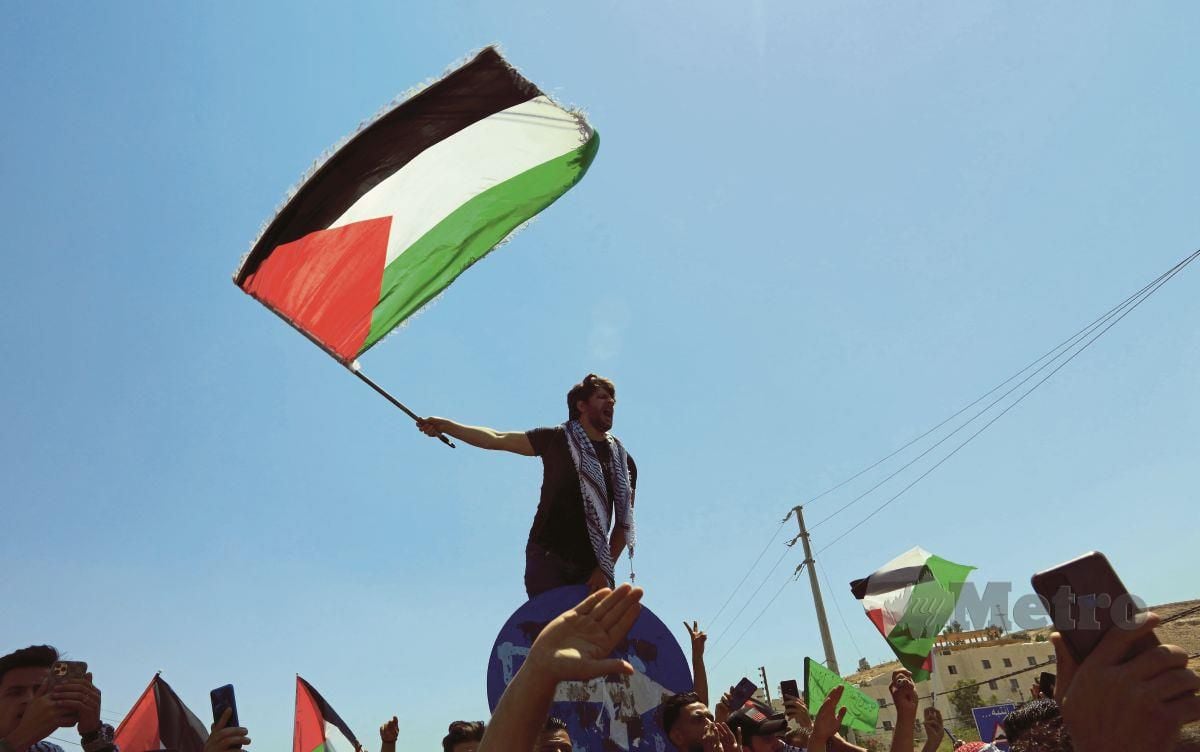 PENUNJUK perasaan mengibarkan bendera Palestin ketika berhimpun di Karameh berdekatan sempadan Palestin - Jordan pada 14 Mei lalu. 2021. FOTO Agensi