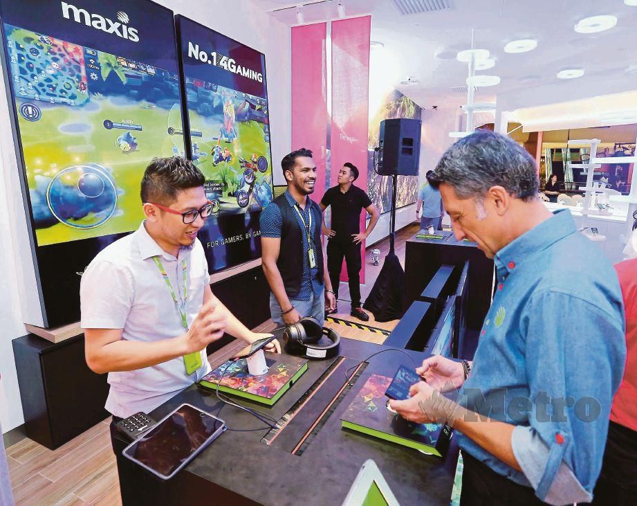 GOKHAN (kanan) mencuba permainan di kedai konsep Maxis di Gardens Mid Valley yang dilancarkan, semalam. FOTO Saifullizan Tamadi