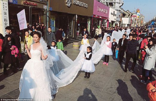PENDUDUK bandar bersama-sama membantu mengangkat leretan gaun pengantin berkenaan.