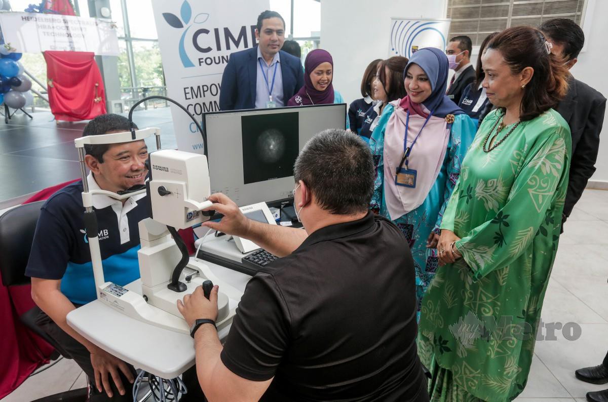 AHMAD Shahriman (kiri) mencuba mesin pengimejan mata terkini bersama Dr Nazirah (kanan), pada majlis penyerahan mesin itu yang disumbangkan Yayasan CIMB, hari ini. FOTO Hazreen Mohamad.