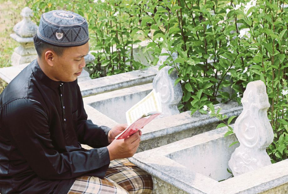 MOHD Firdaus  membaca surah Yasin di pusara ahli keluarganya  di Tanah Perkuburan Islam Kampung Cherang Melintang.