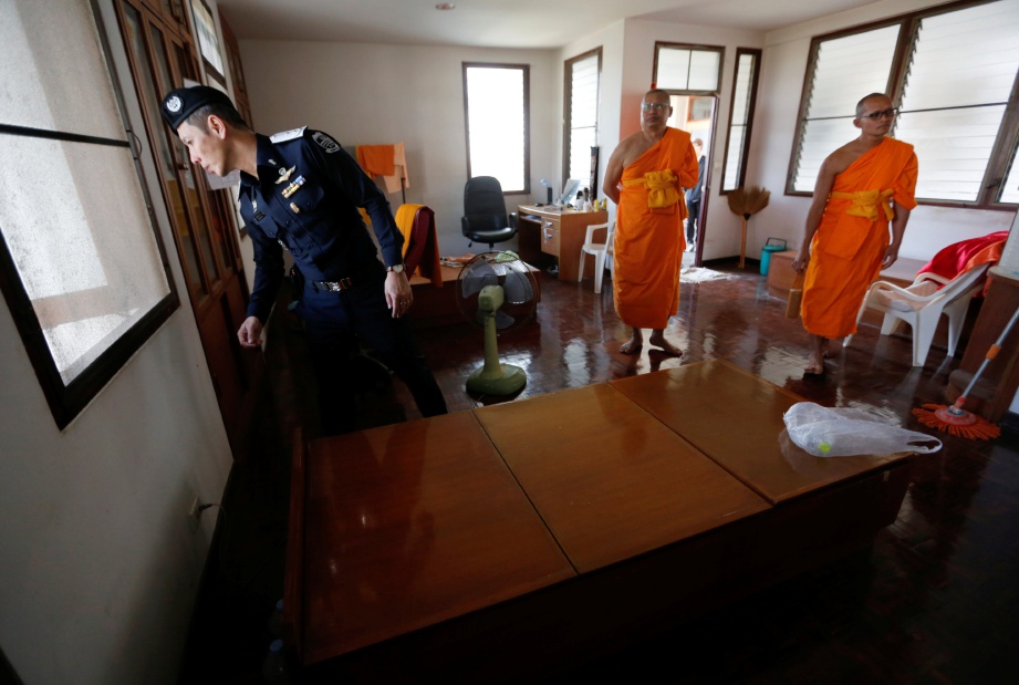 SEORANG anggota polis memeriksa sebuah bilik di kuil Dhammakaya di wilayah Pathum Thani sambil diperhatikan dua sami.  - Reuters 