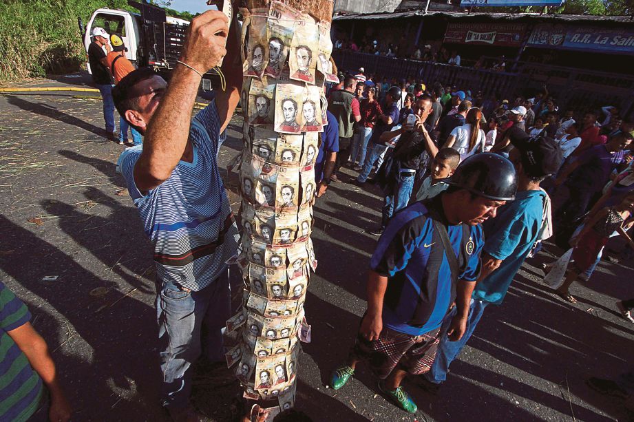 PENDUDUK menampal wang kertas 100 bolivar di sebatang tiang sebagai membantah kekurangan wang tunai di bandar San Cristoba, Venezuela kelmarin. - AFP