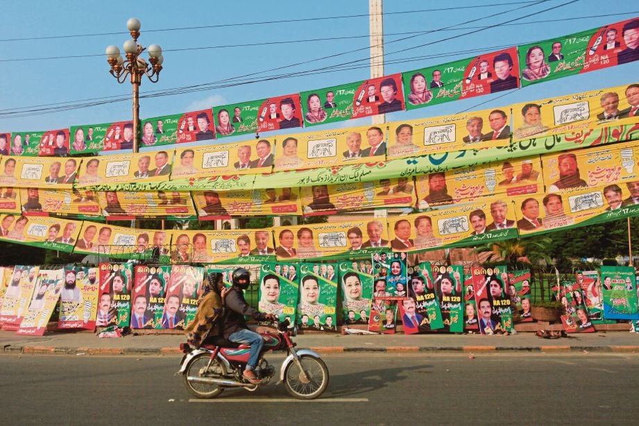 PENUNGGANG motosikal melalui sebatang jalan yang penuh dengan poster pilihan raya di Lahore, Pakistan semalam. - Reuters