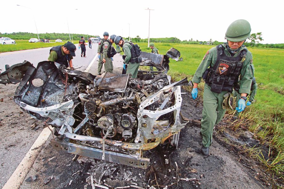 ASKAR memeriksa kenderaan yang musnah selepas dicuri sebelum diletupkan di sebatang jalan di wilayah Pattani kelmarin. - Reuters