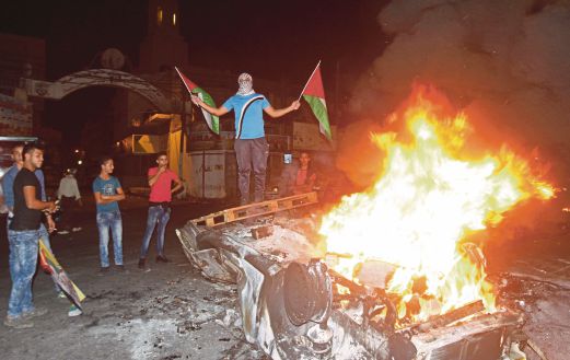 SEORANG lelaki memegang bendera Palestin berdiri di atas kereta milik penjajah Yahudi yang dibakar selepas cuba masuk ke tempat suci secara haram.