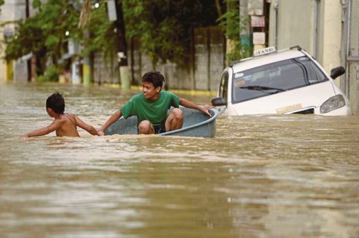 DUA kanak-kanak menggunakan besin untuk meredah jalan raya yang dinaiki air di Candaba, Pampanga di utara Manila, semalam. 