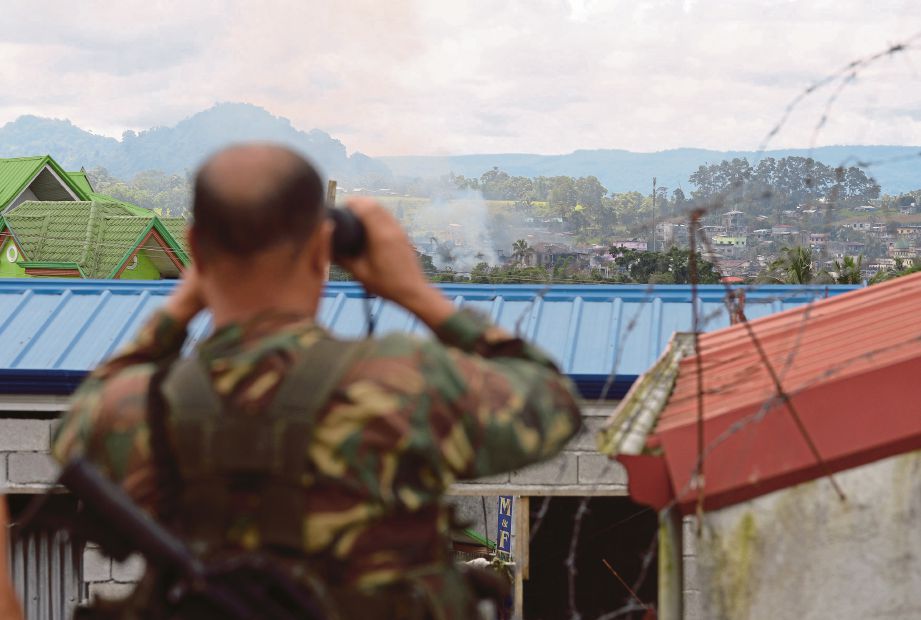 SEORANG askar menggunakan teropong untuk melihat kedudukan militan di tengah bandar Marawi yang dibom pesawat tentera. - AFP