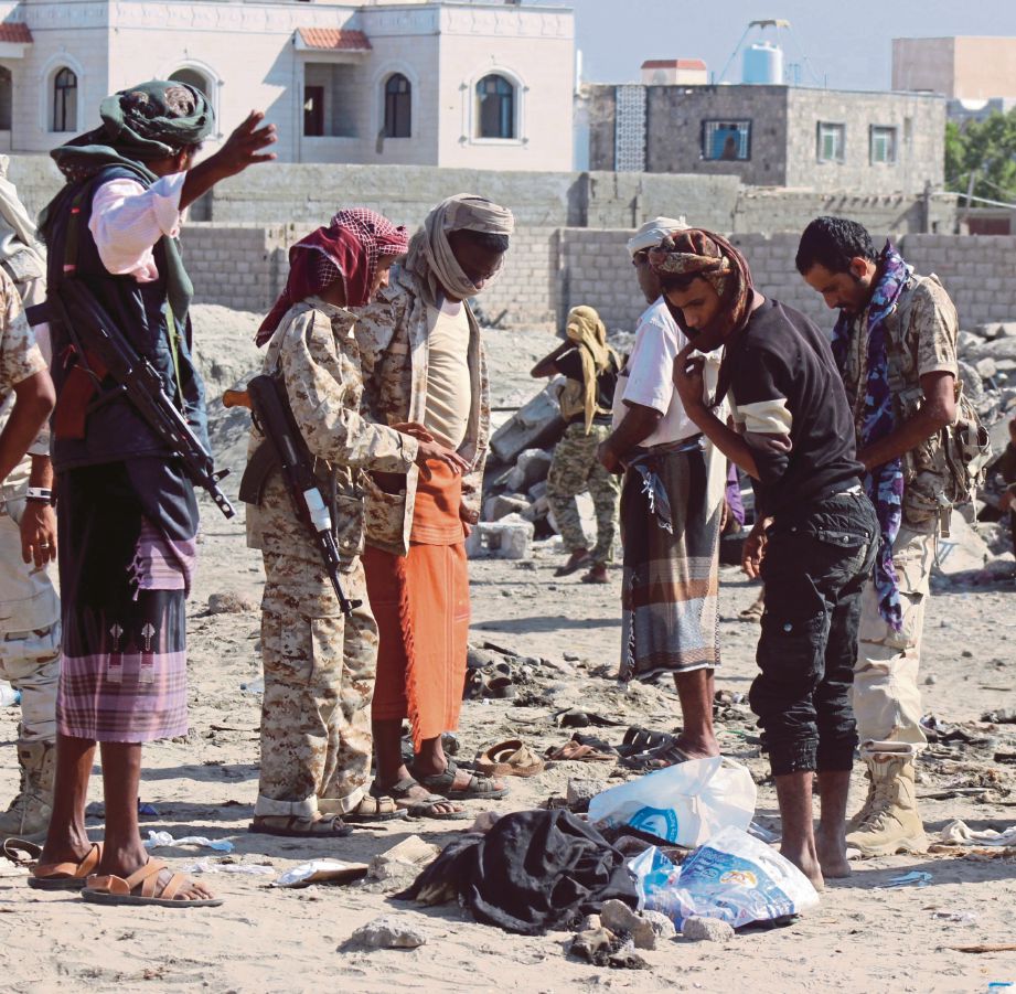 PENDUDUK dan lelaki bersenjata memeriksa kawasan serangan di sebuah pangkalan tentera di Aden.   - EPA