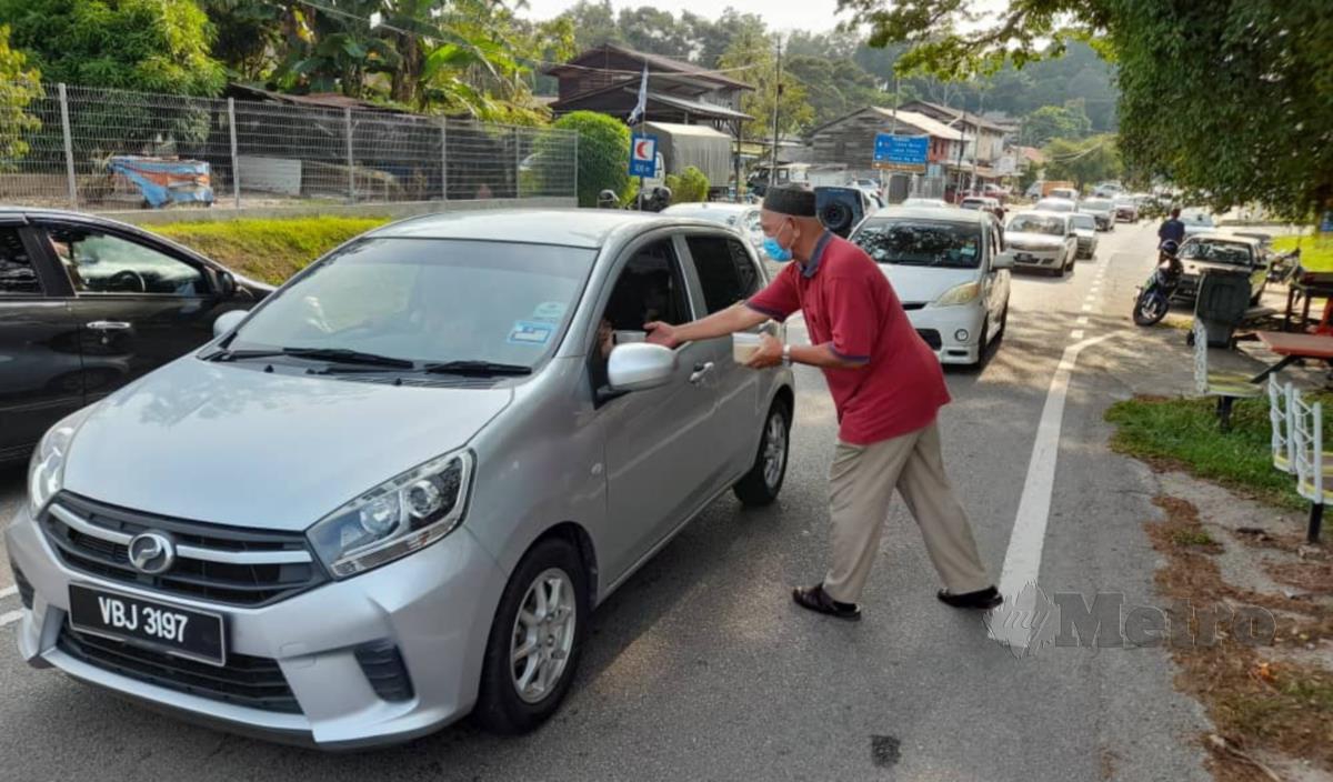 Abdul Razak menghulurkan bubur lambuk kepada pengguna jalan raya di Kampung Bukit Beringin, Masjid Tanah. FOTO HASSAN OMAR