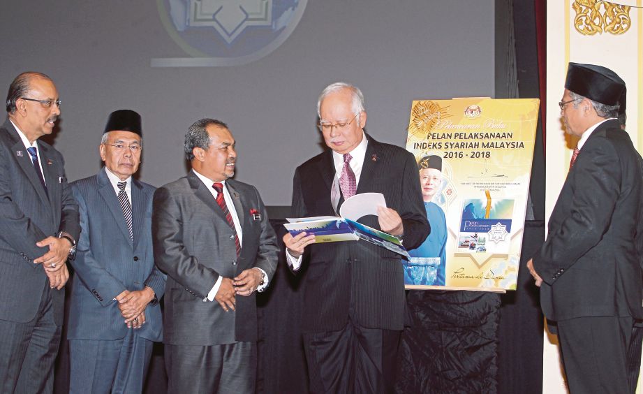 NAJIB  melihat Buku Pelan Pelaksanaan Indeks Syariah Malaysia 2016-2018 di Kompleks Seri Perdana, Putrajaya sambil diperhatikan  Jamil Khir dan  Pengerusi Majlis Fatwa Kebangsaan, Prof Emeritus Tan Sri Dr Abdul Shukor Husin.
