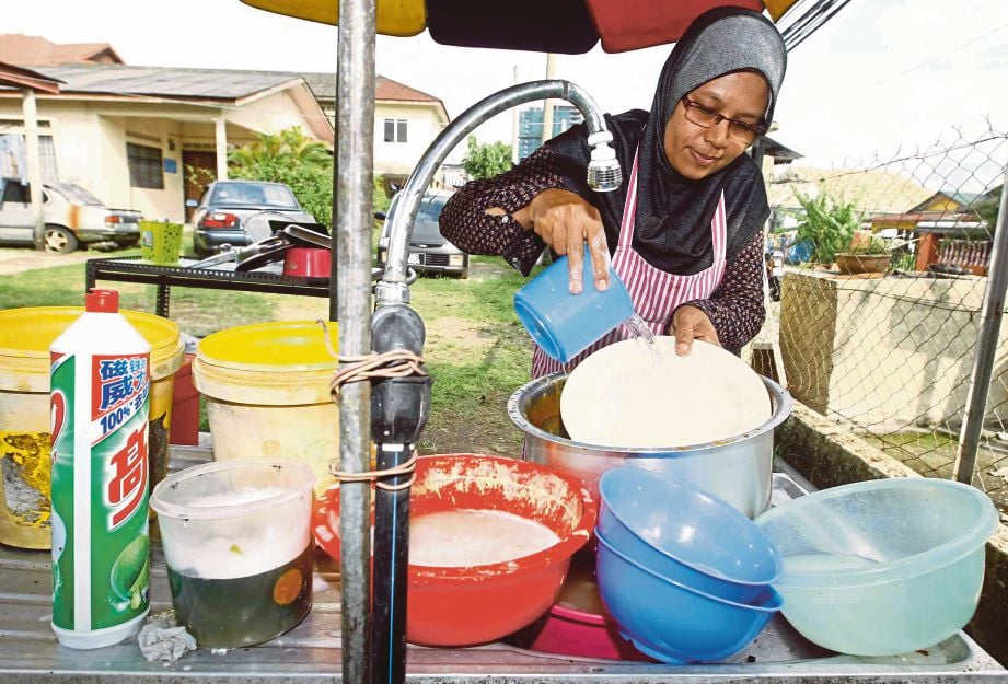 PENIAGA membasuh mangkuk menggunakan air tadahan yang disimpan sebelum berlaku gangguan bekalan air di gerainya Kampung Malaysia Raya.