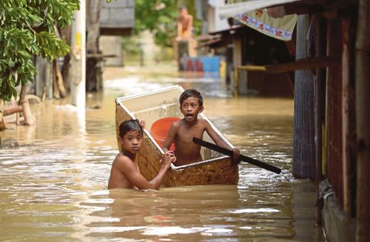 DUA kanak-kanak menggunakan peti sejuk yang sudah tidak boleh digunakan untuk meredah banjir di Candaba, Pampanga, utara Manila, semalam. 