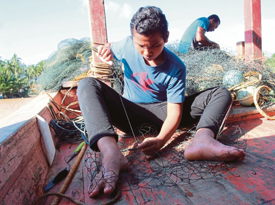 HASRUL membantu bapanya, Ismail mengambil upah menjahit pukat nelayan di Teluk Buaya, Pantai Mek Mas. FOTO Bernama