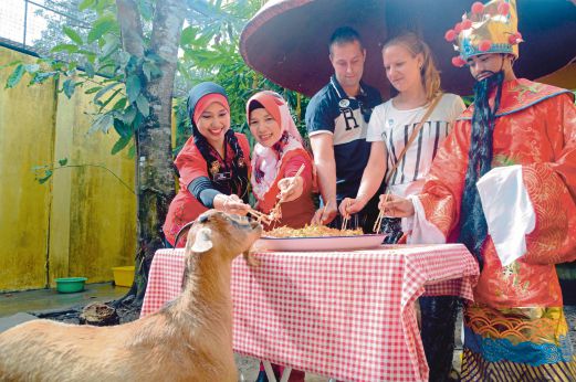 NUR Hamzani (kiri) bersama dua pelancong asing menggaul Yee Sang sebelum diberikan kepada kambing jinak, Memey pada gimik sambutan Tahun Baru Cina.