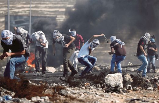 REMAJA Palestin berlindung selepas menyerang tentera Israel dengan batu dari belakang tayar yang dibakar ketika pertempuran di bandar Al-Bireh, utara Ramallah, di Tebing Barat,  semalam. 