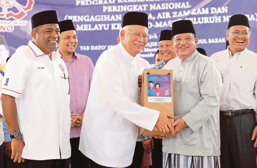 NAJIB  menyampaikan sumbangan kurma, air zamzam dan kain baju Melayu kepada Tengku Adnan (kanan) pada Majlis Pelancaran Program Ramadan Al-Mubarak peringkat nasional di Masjid Negara, semalam sambil disaksikan Abdul Azeez (kiri).