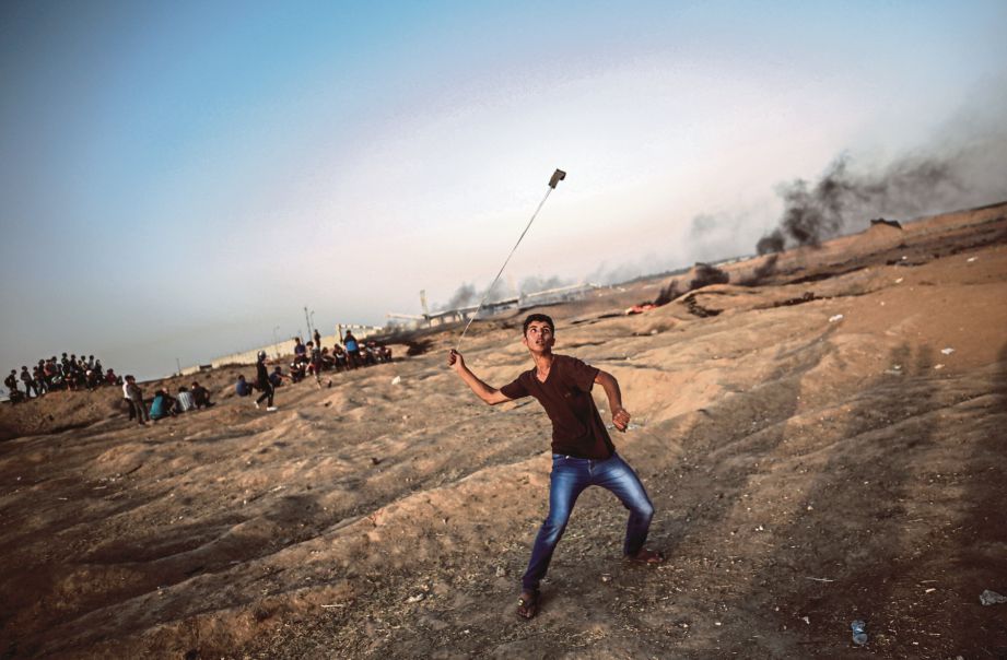 SEORANG remaja Palestin membaling batu ketika bertempur dengan tentera Israel di sempadan Gaza pada Jumaat lalu. - EPA