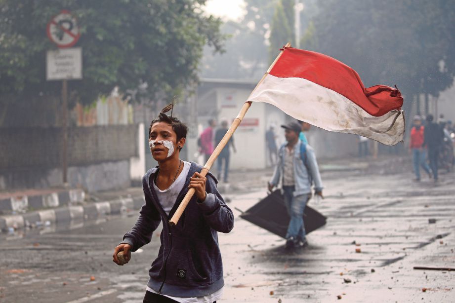 SEORANG penunjuk perasaan berlari sambil membawa bendera Indonesia. FOTO Reuters