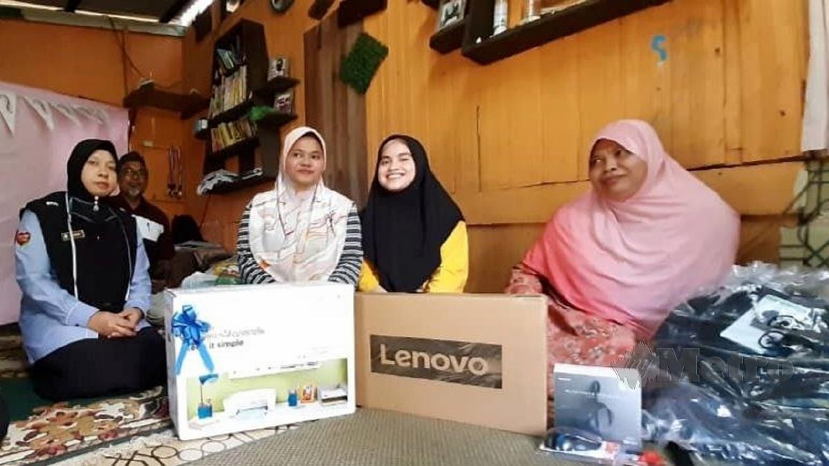 SITI Nurakma (dua kiri) dan Siti NurNajwa (dua kanan) menerima sumbangan komputer riba dan alat pencetak serta keperluan pembelajaran dan wang tunai daripada Farihah (kiri) sambil diperhatikan Suparmiyati. FOTO Zaid Salim
