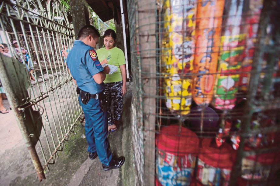 SEORANG anggota polis mengambil butiran peribadi seorang penduduk di Payatas sebelum ujian saringan dadah dilakukan. - Agensi