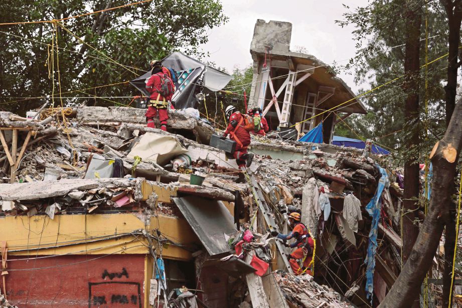 ANGGOTA penyelamat mencari mangsa di celah runtuhan rumah. - Reuters  