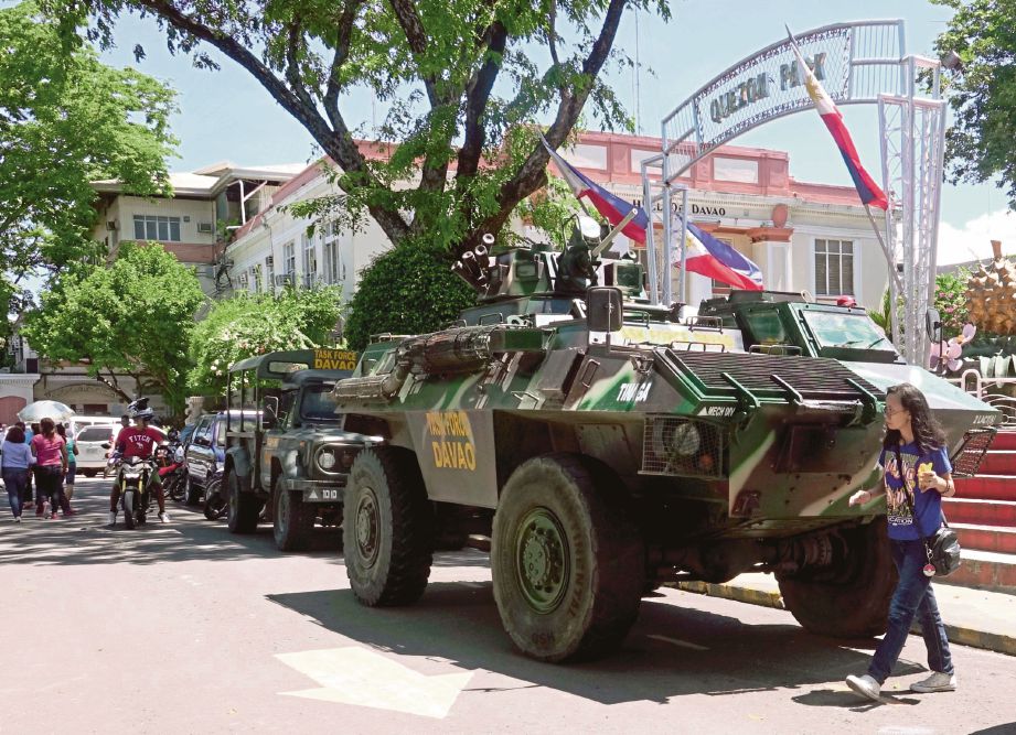 PENDUDUK di bandar Davao di Mindanao berjalan melintasi kenderaan tentera selepas Duterte mengisytiharkan penguatkuasaan undang-undang tentera di Mindanao.  - EPA 