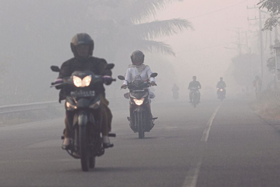 PENDUDUK menunggang motosikal meredah jerebu yang berpunca daripada kebakaran tanah gambut di Kampung Suak Raya, Aceh Barat, semalam.  - Antara 