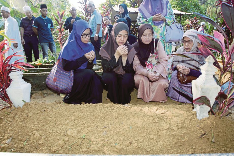 Roziah  (dua dari kiri) di pusara suaminya sambil ditemani ahli keluarga di Tanah Perkuburan Islam Kampung Pulau Rusa.